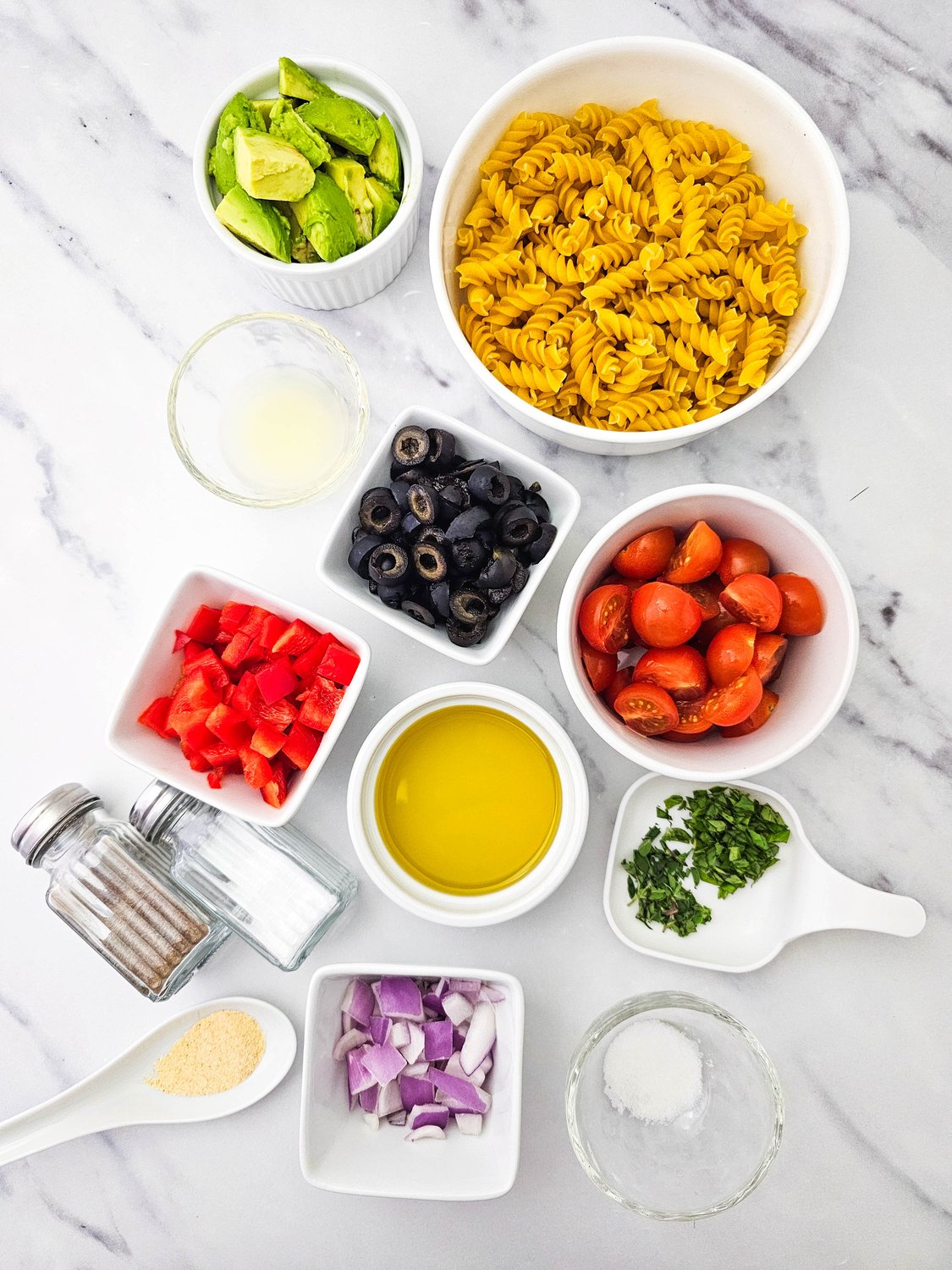 Ingredients for vegan pasta salad: pasta, cherry tomatoes, olives, avocado, peppers, and herbs