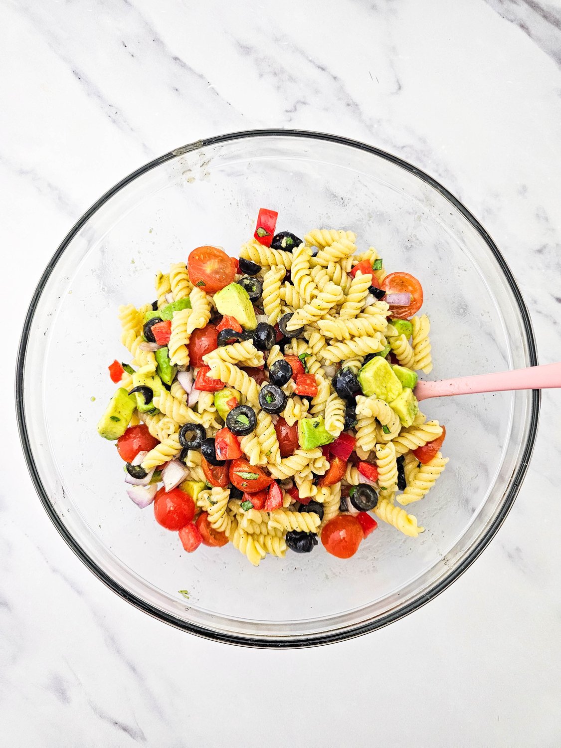 Vegan pasta salad tossed together in a glass mixing bowl