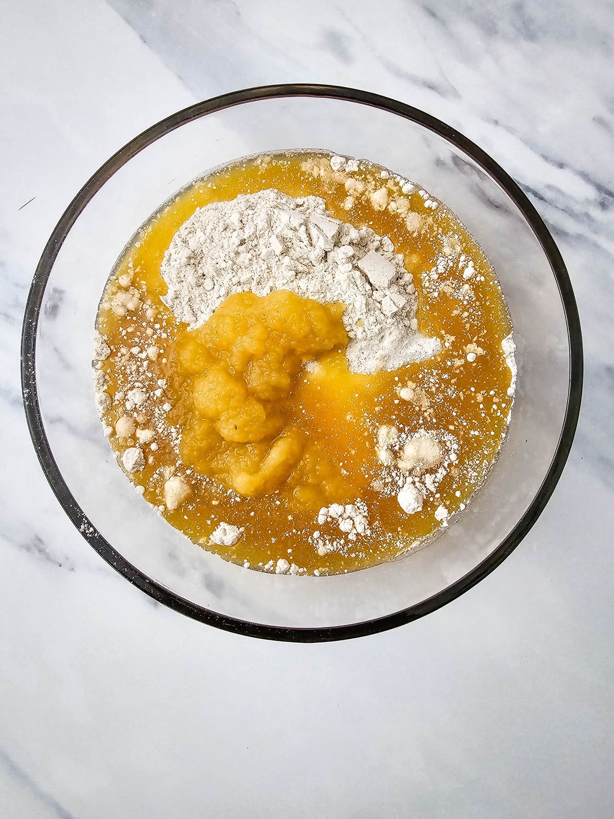 Apple cider poured into the cake mix and applesauce in a glass bowl