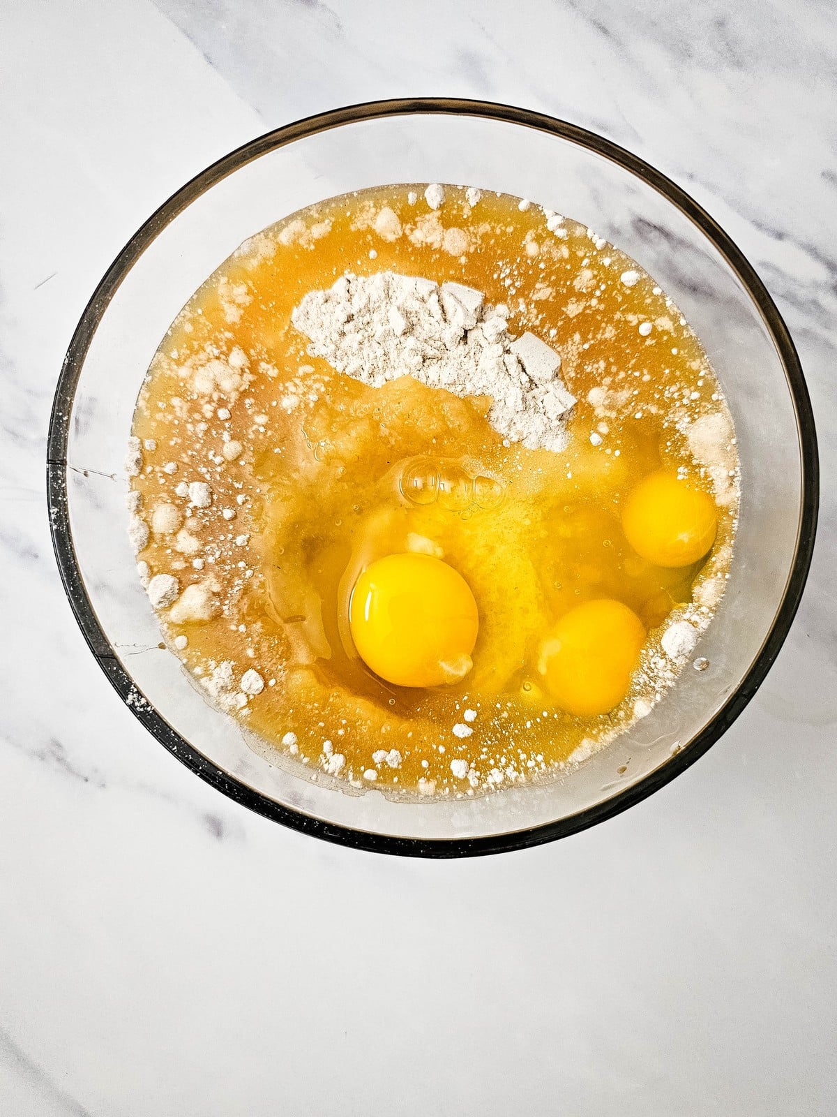 Three eggs cracked into the apple cider donut batter in a glass bowl