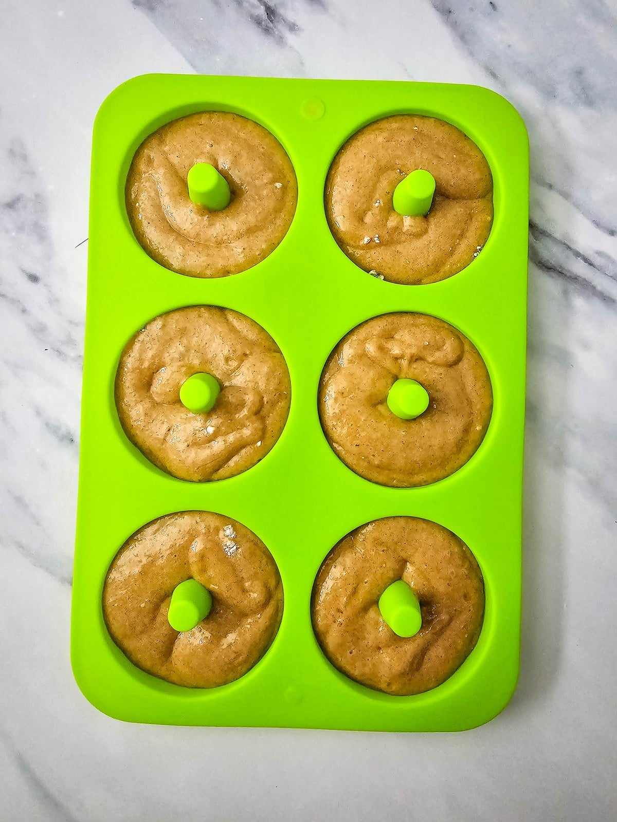 Apple cider donut batter piped into a green silicone donut mold