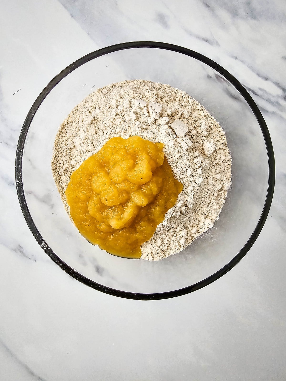 Spice cake mix and applesauce in a glass mixing bowl for apple cider donuts