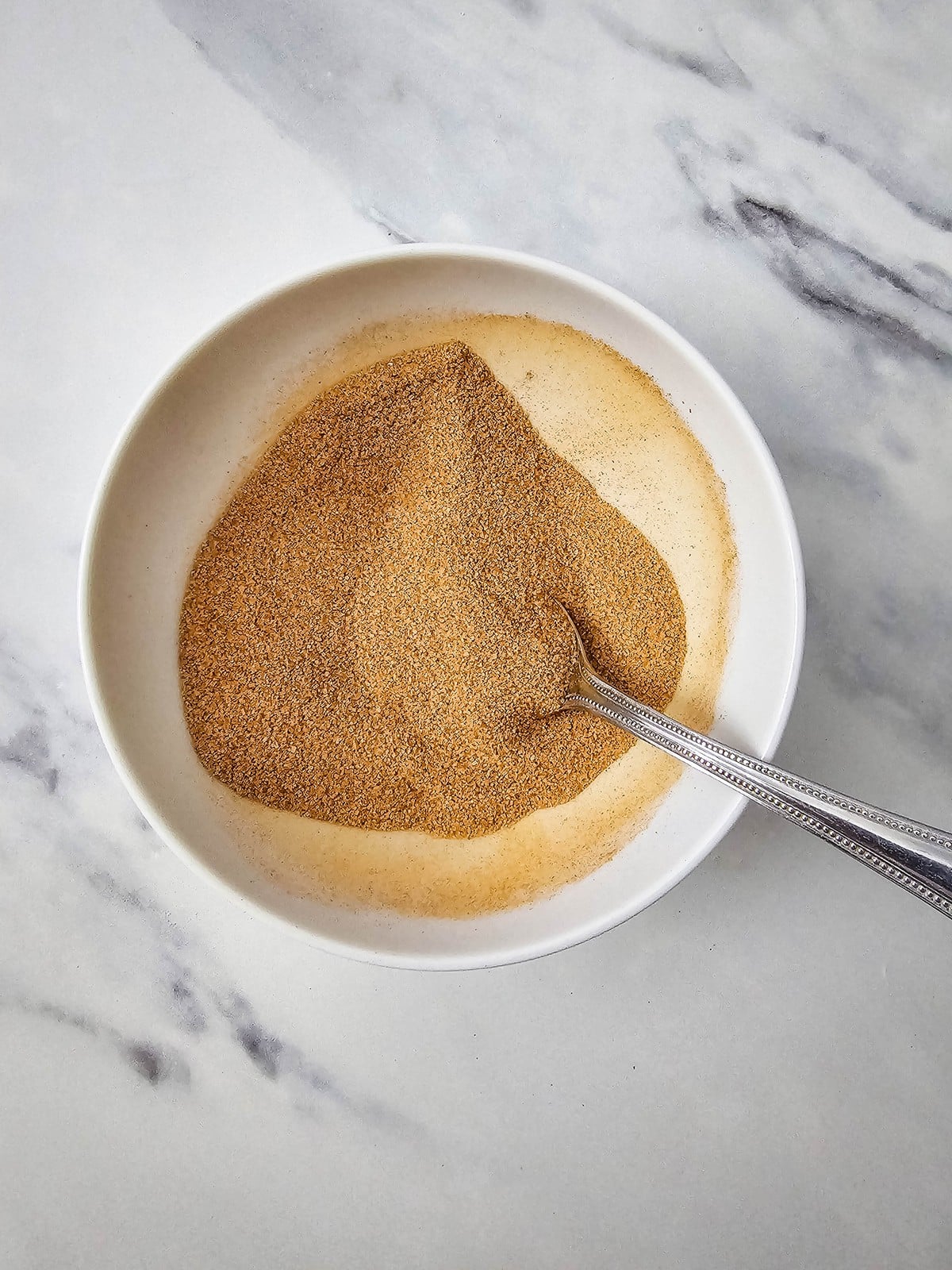 Cinnamon and sugar stirred together in a white bowl for coating apple cider donuts