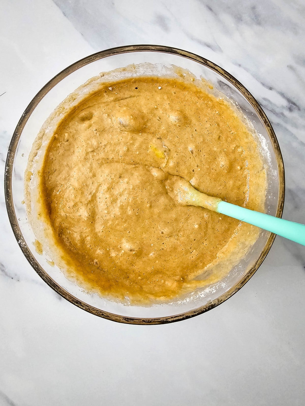 Smooth apple cider donut batter mixed with a spatula in a glass bowl