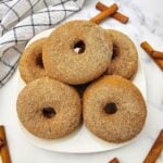 Overhead view of baked apple cider donuts rolled in cinnamon sugar on a white plate