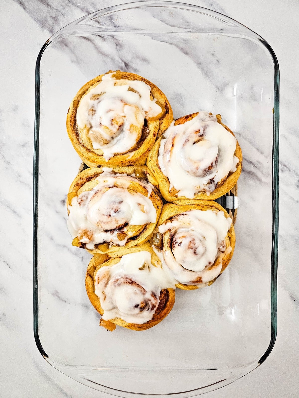 Baked apple cinnamon rolls in the dish with icing spread over the tops