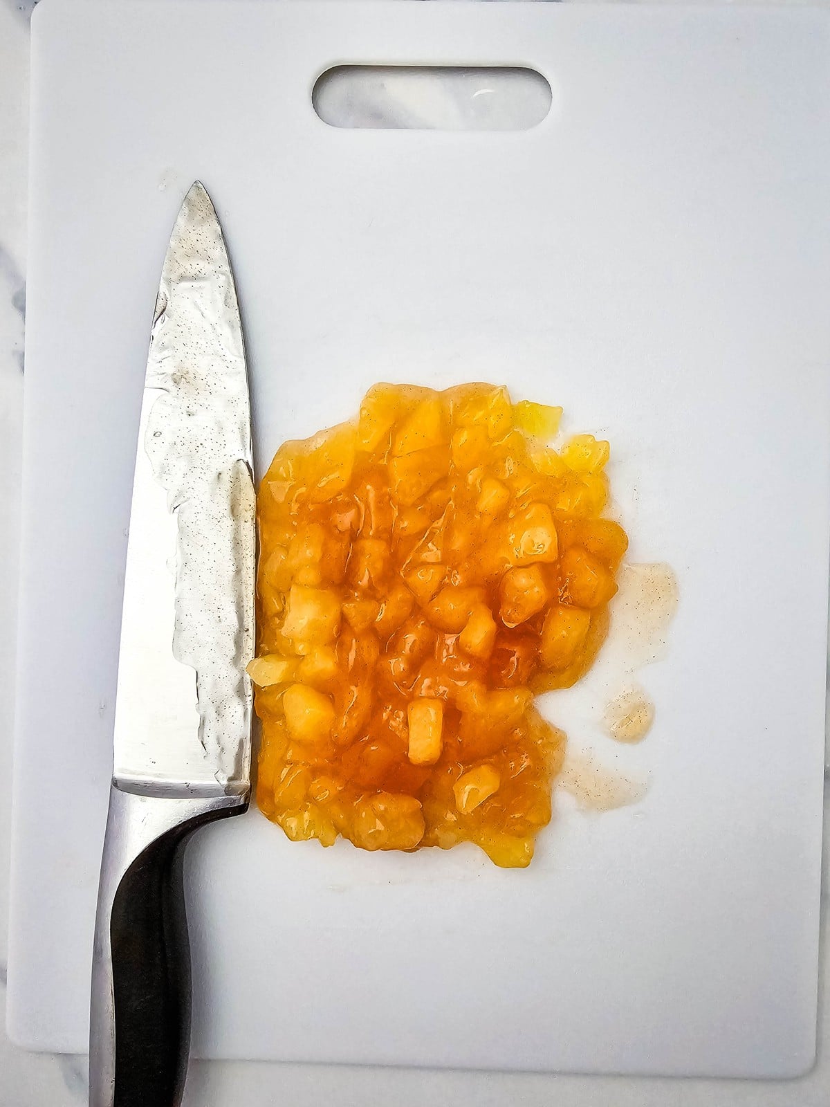 Chopped apple pie filling on a white cutting board with a chef knife
