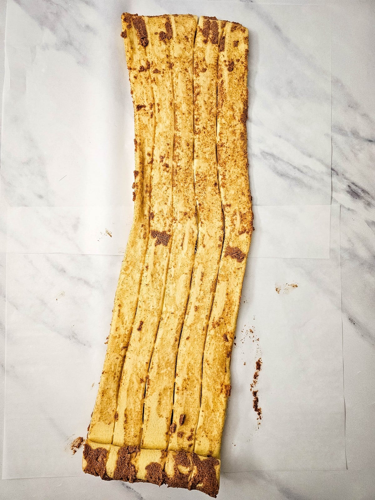 Cinnamon roll dough unrolled into long flat strips on parchment