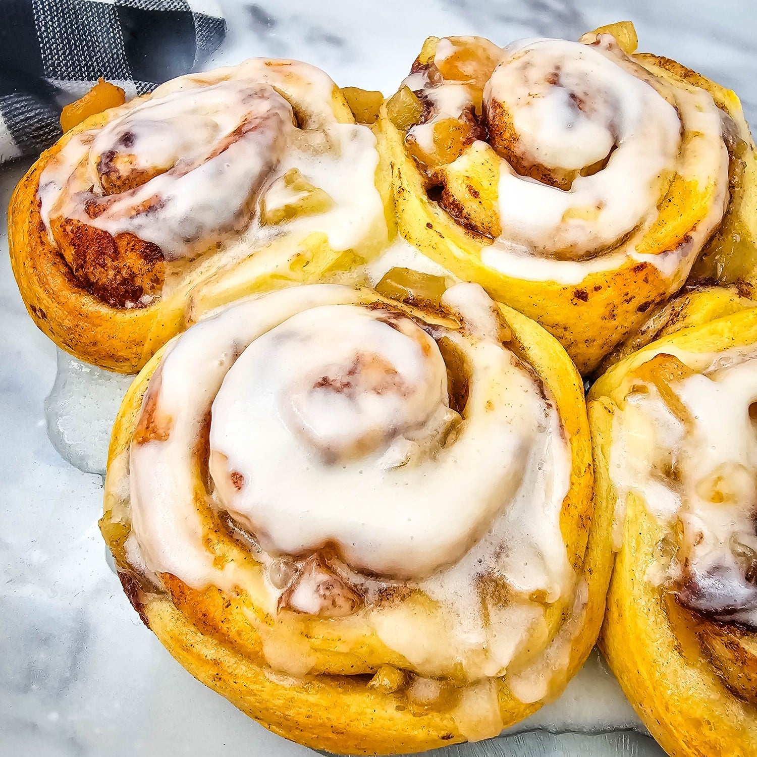Iced apple cinnamon rolls in a baking dish with apple pie filling showing through the spirals