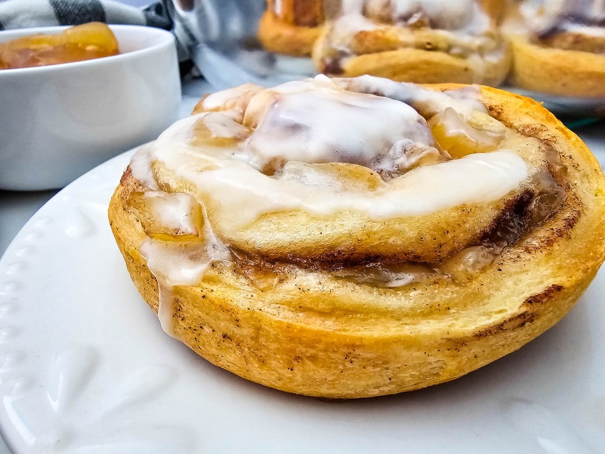 Close up of a single iced apple cinnamon roll on a white plate