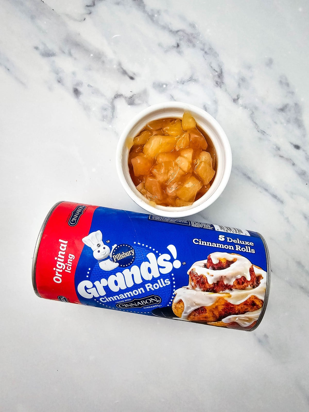 Tube of Pillsbury Grands cinnamon rolls beside a bowl of chopped apple pie filling
