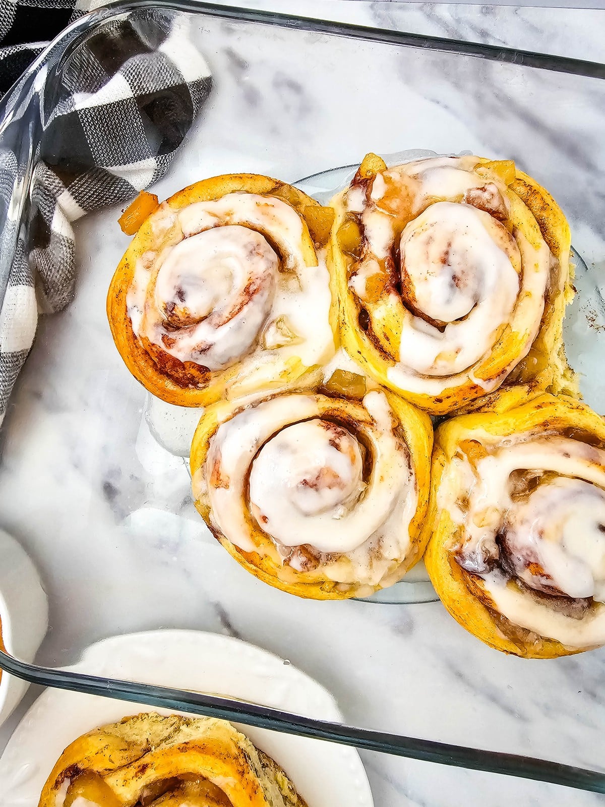 Overhead view of four iced apple cinnamon rolls in a glass baking dish