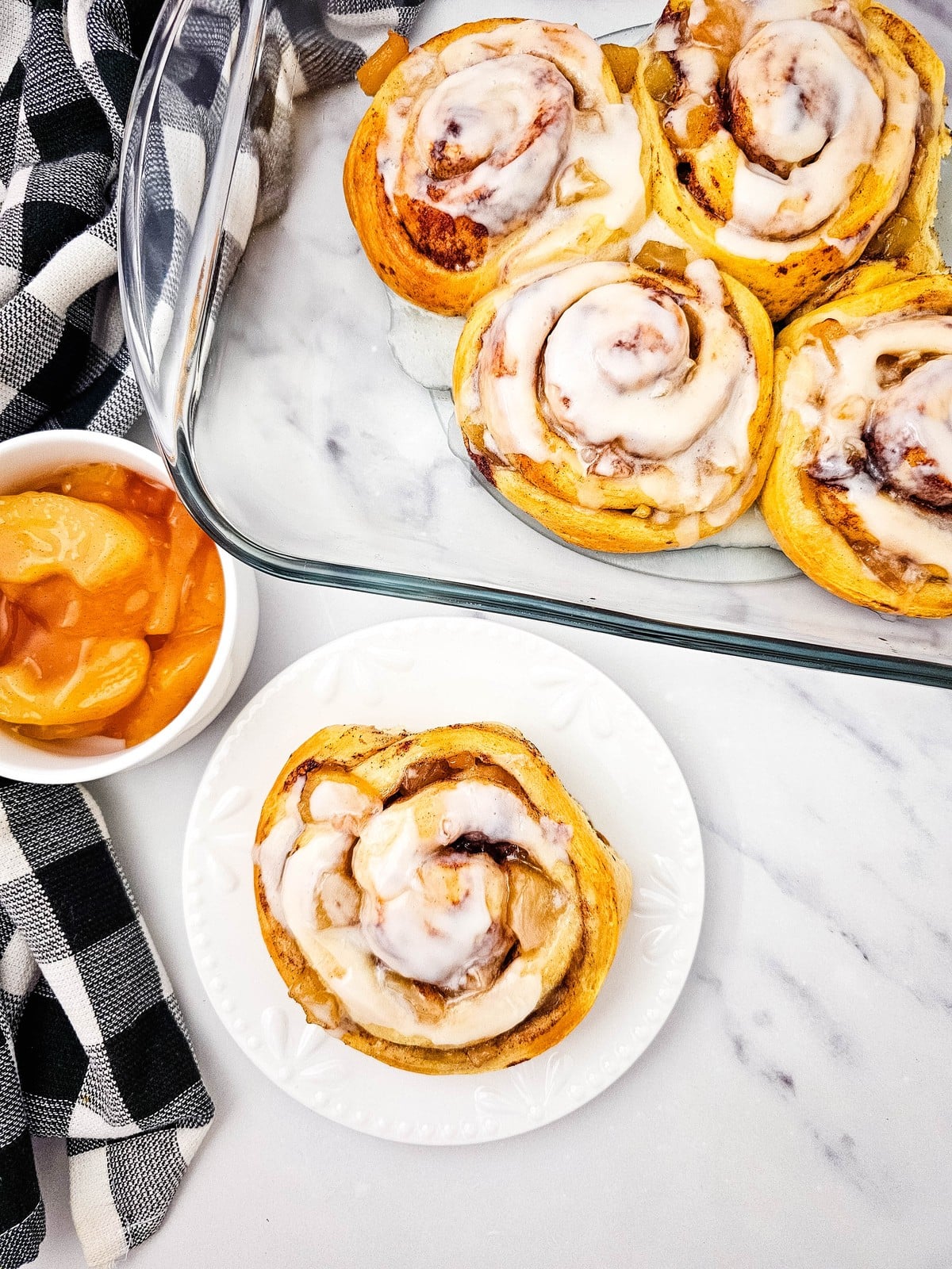 Apple cinnamon roll on a white plate beside the baking dish and a bowl of apple pie filling