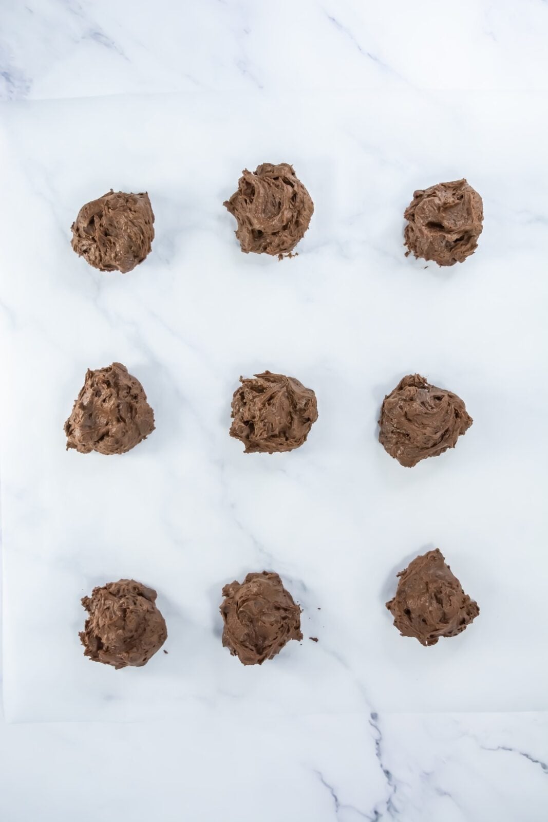 Scoops of brownie cookie dough spaced on a parchment-lined baking sheet