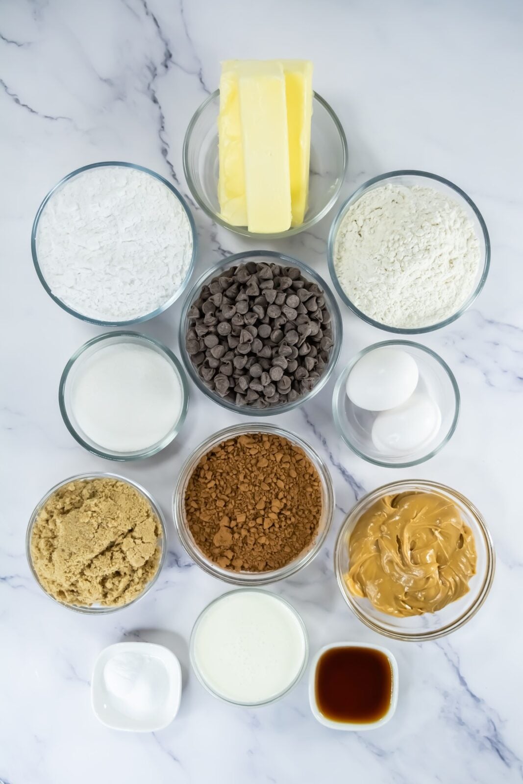 Ingredients for buckeye brownie cookies laid out in bowls including cocoa, sugars, peanut butter, and chocolate chips