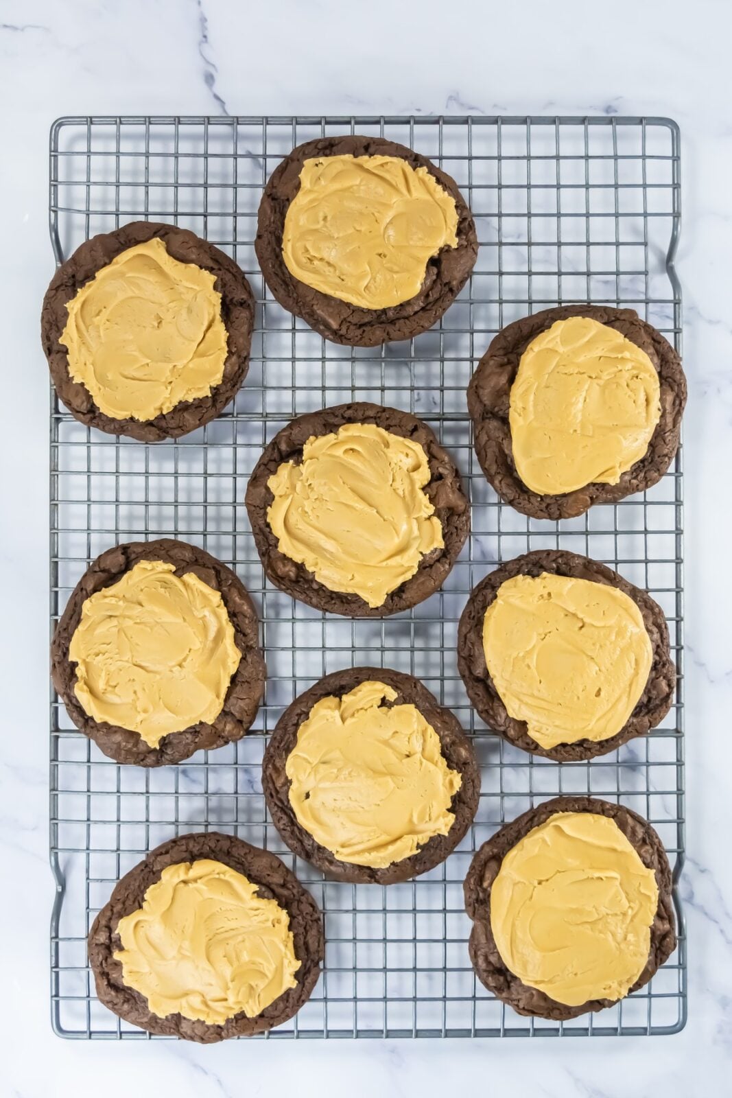 Brownie cookies topped with a layer of peanut butter filling on a wire rack