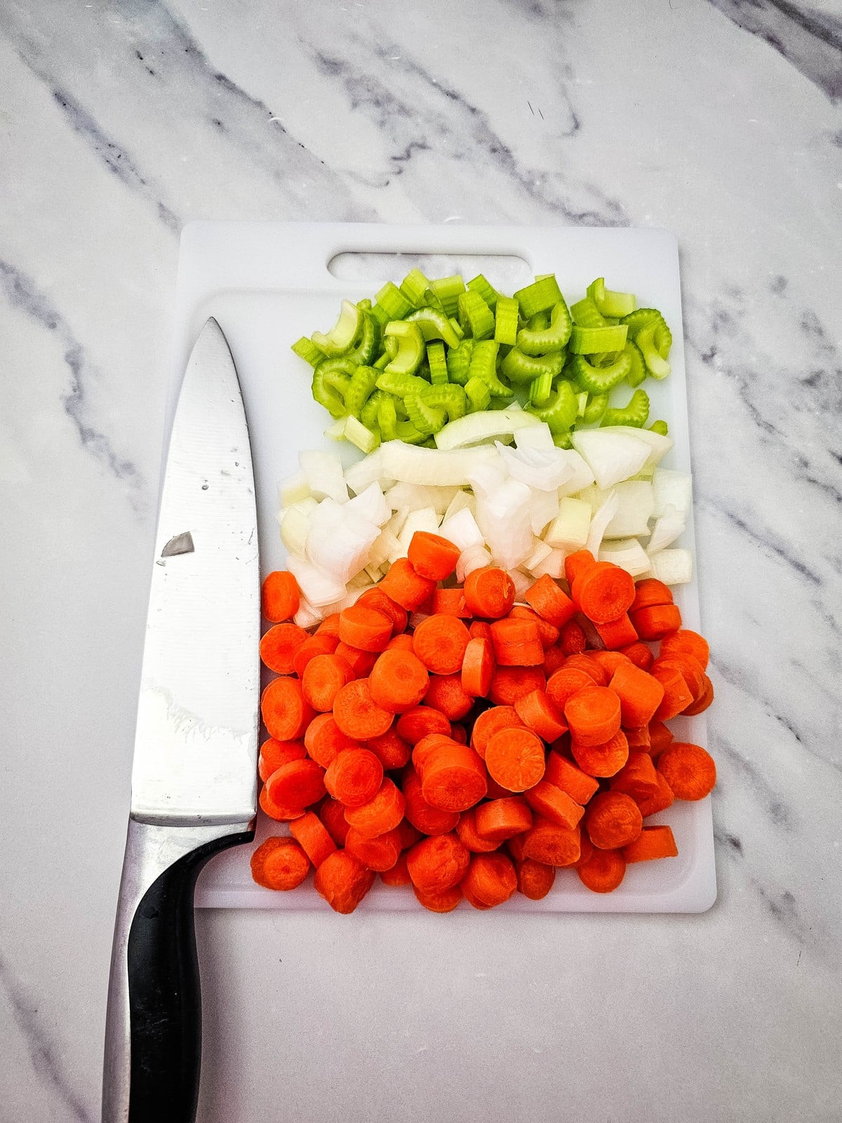 chopped celery, onion and sliced carrots on a cutting board with a knife