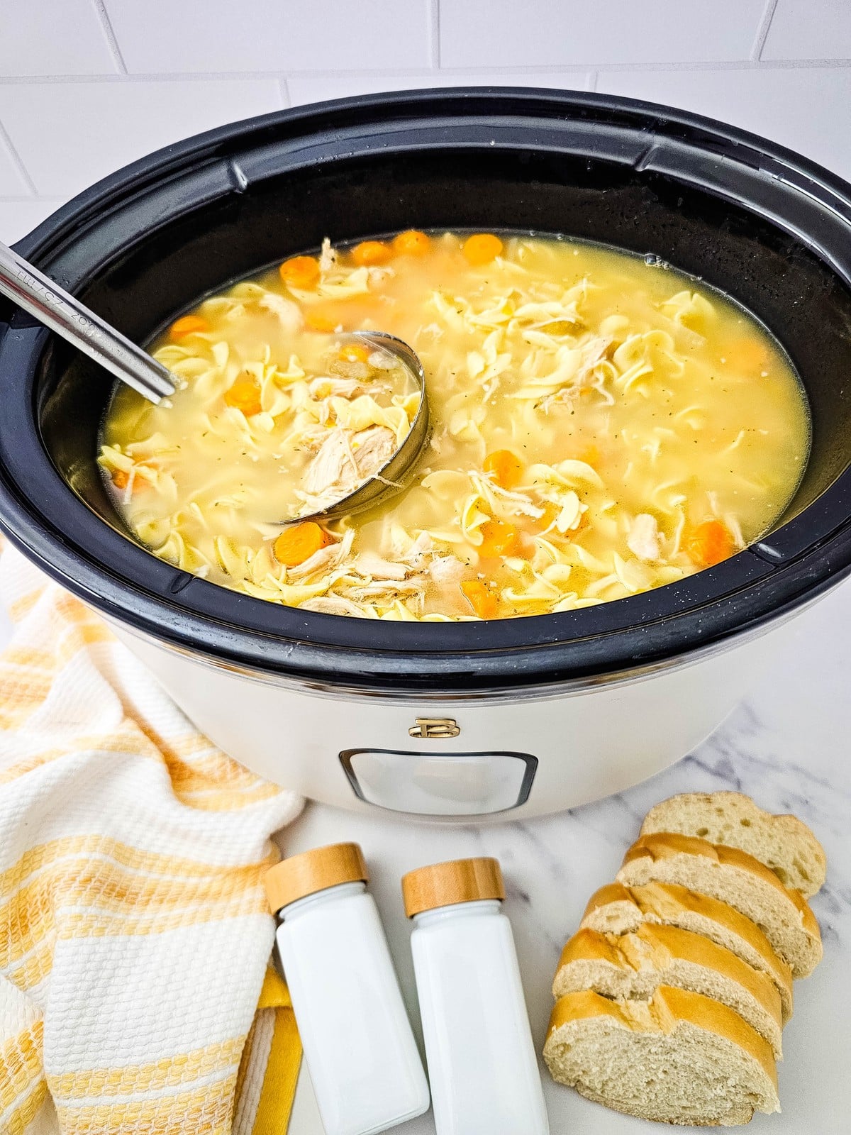 the finished soup in the crockpot with a ladle, bread and salt and pepper shakers alongside