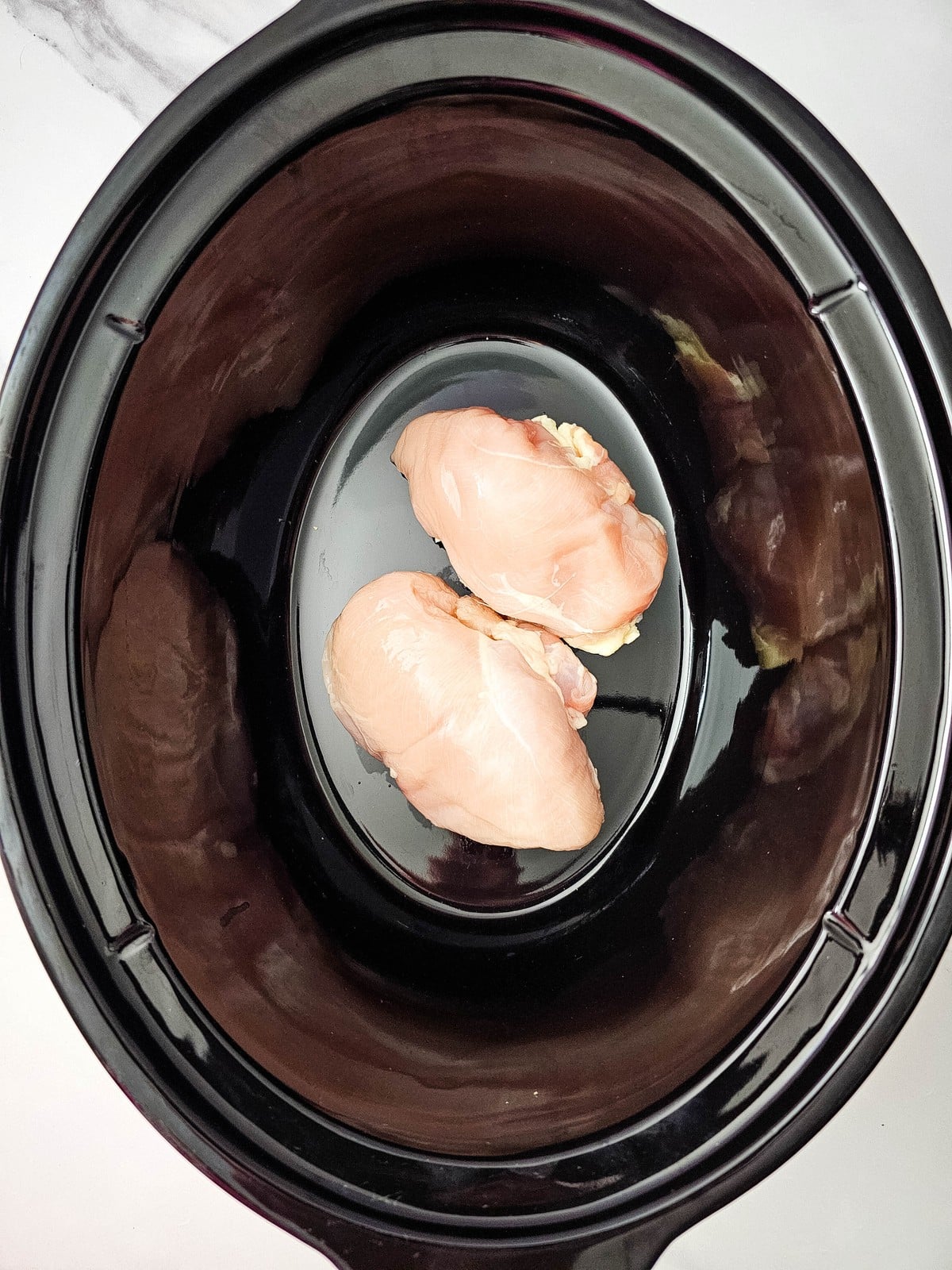 two raw chicken breasts in the bottom of the crockpot