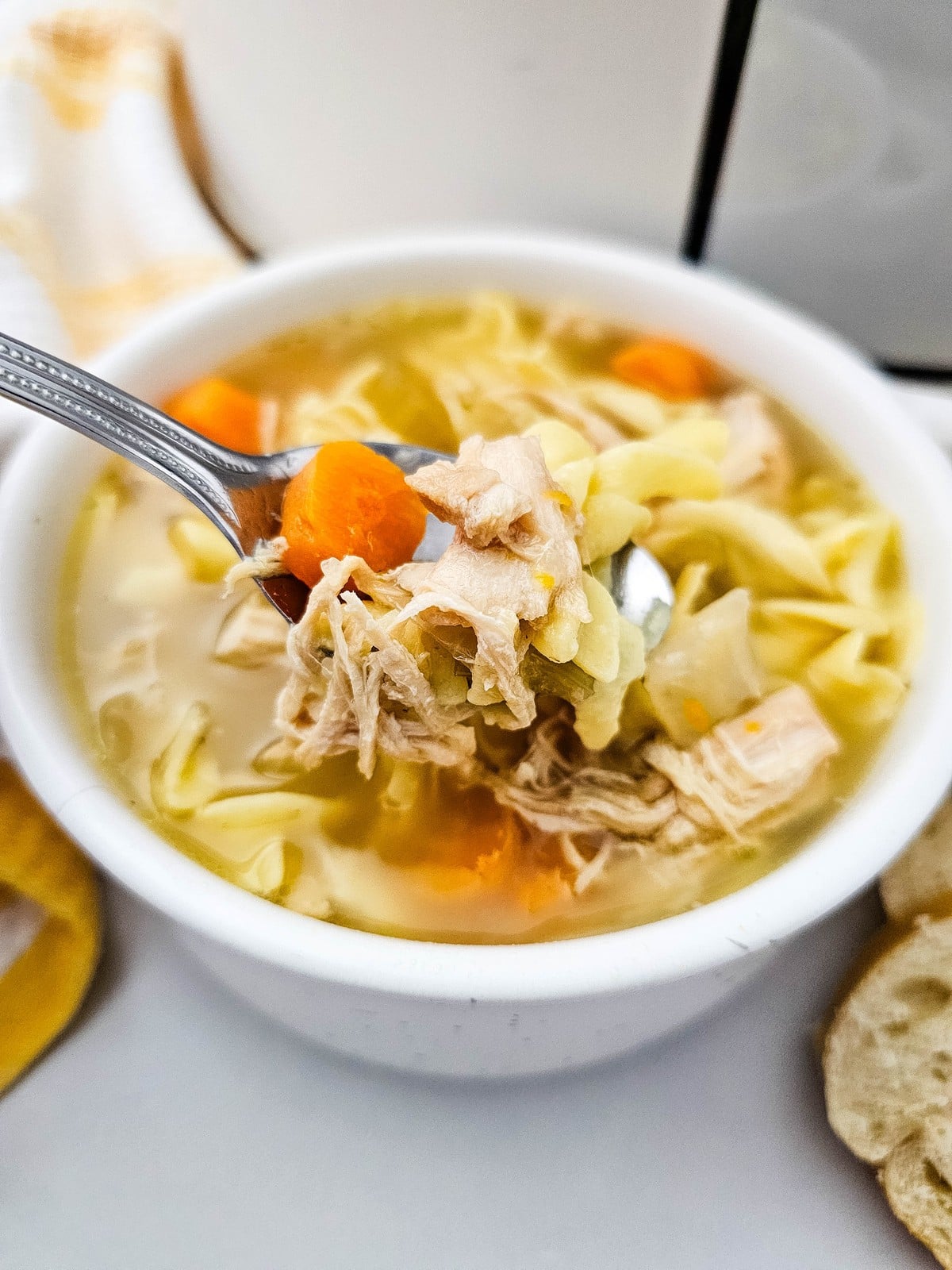 a spoonful of shredded chicken, noodles and carrot lifted out of the bowl