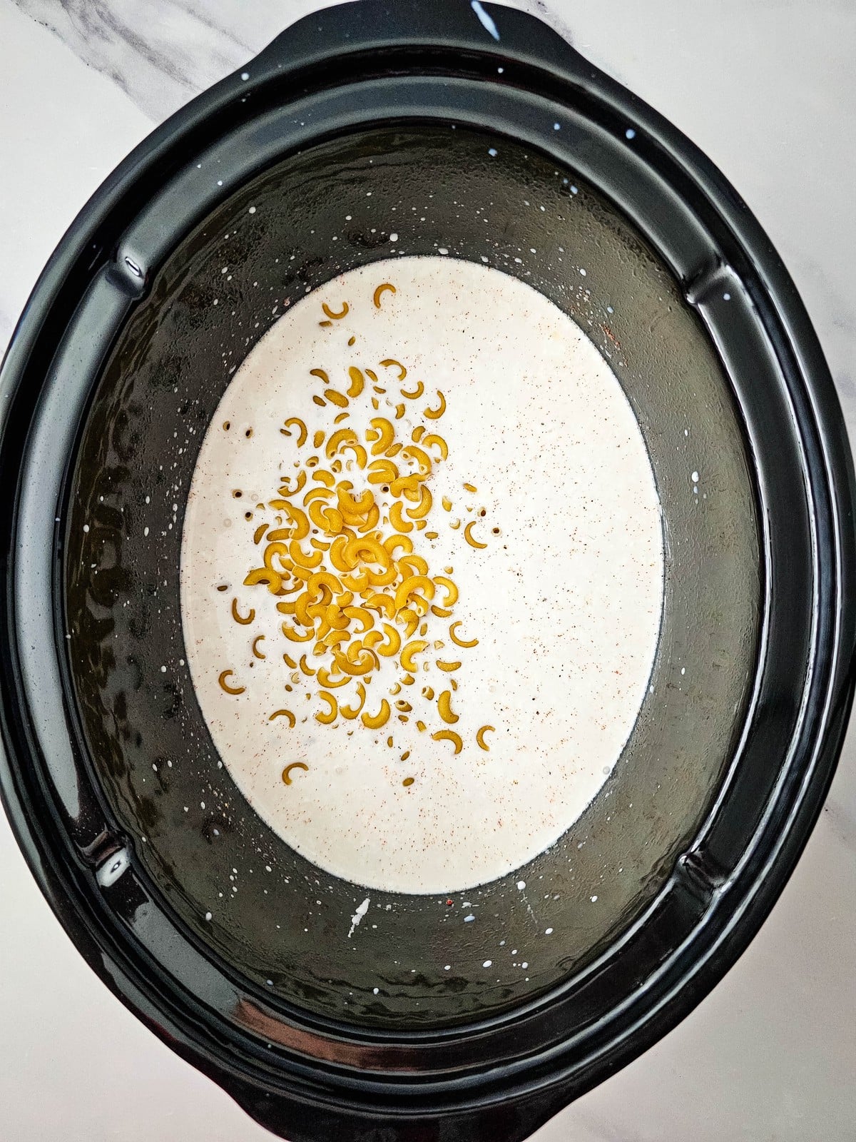 Dry elbow macaroni added to the cream mixture in the slow cooker