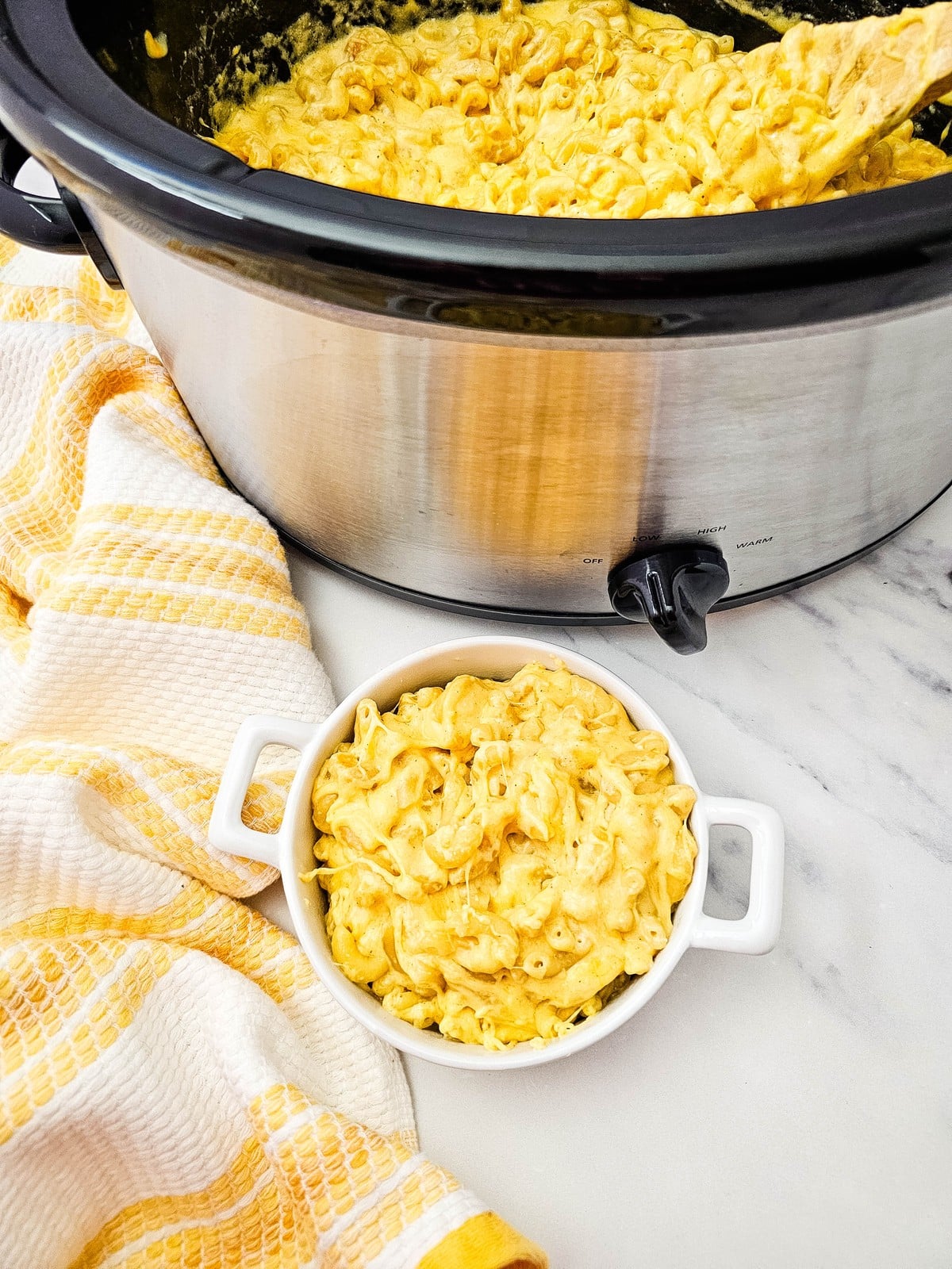 Crockpot mac and cheese in a white bowl beside the slow cooker