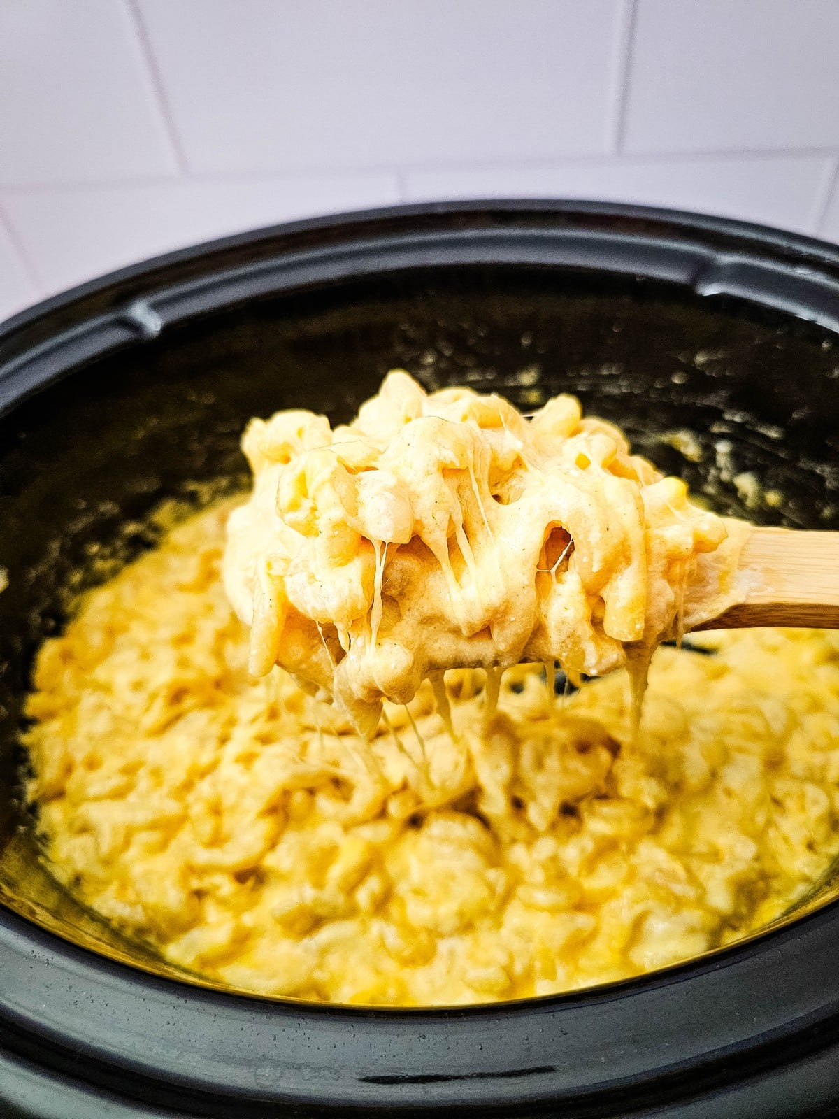 Wooden spoon lifting a cheesy scoop of mac and cheese from the slow cooker