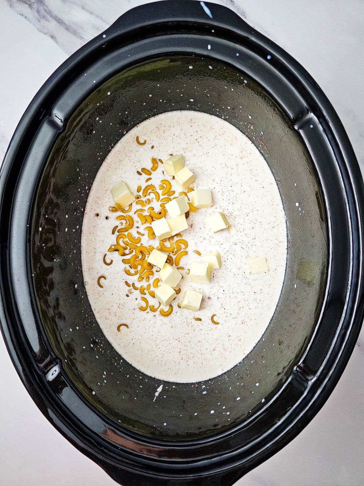 Cubed butter scattered over the macaroni in the slow cooker