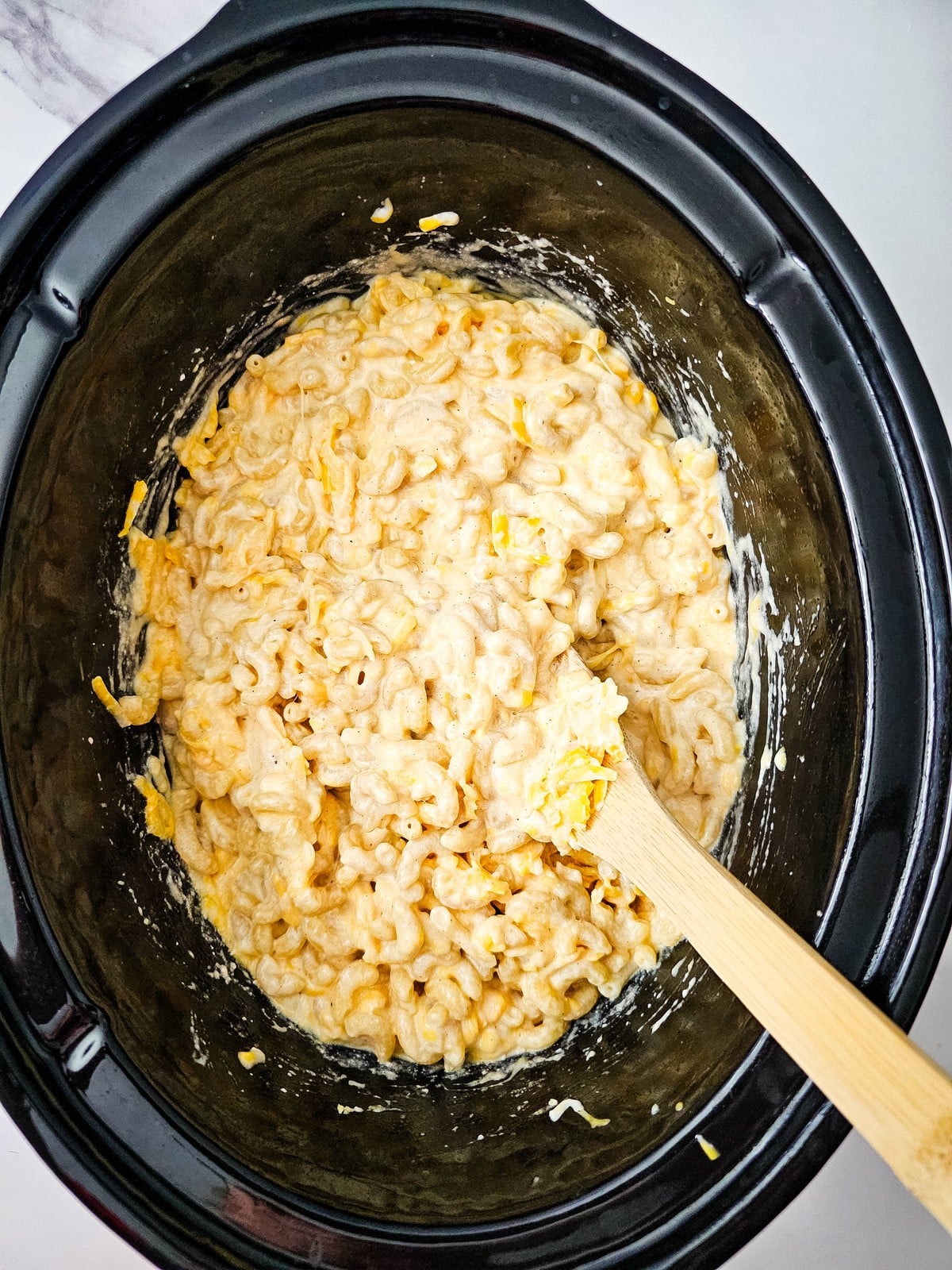 Stirred crockpot mac and cheese coated in melted cheese
