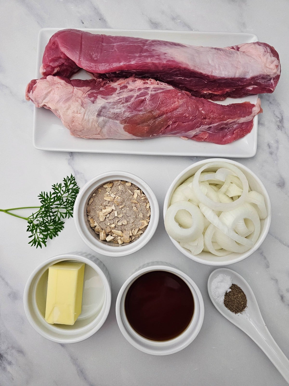 everything you need laid out: two raw pork tenderloins, sliced onion, butter, beef broth, mushroom gravy mix, salt, pepper and parsley