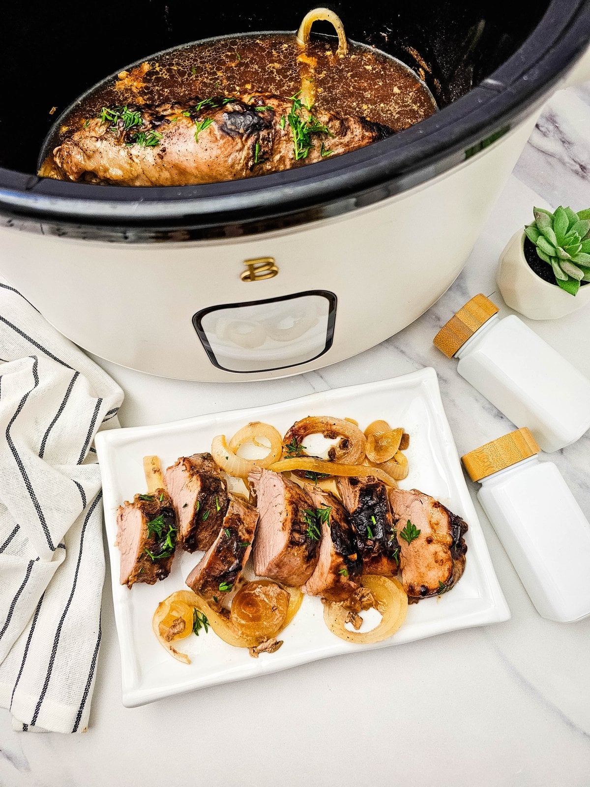 sliced crockpot pork tenderloin on a serving platter next to the slow cooker