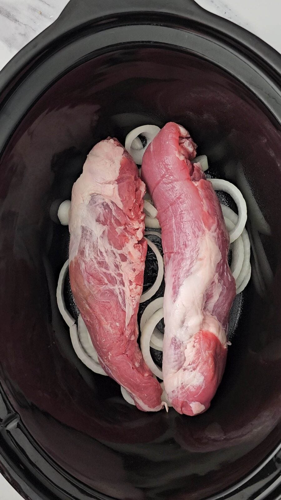 the two raw pork tenderloins laid side by side on top of the onions