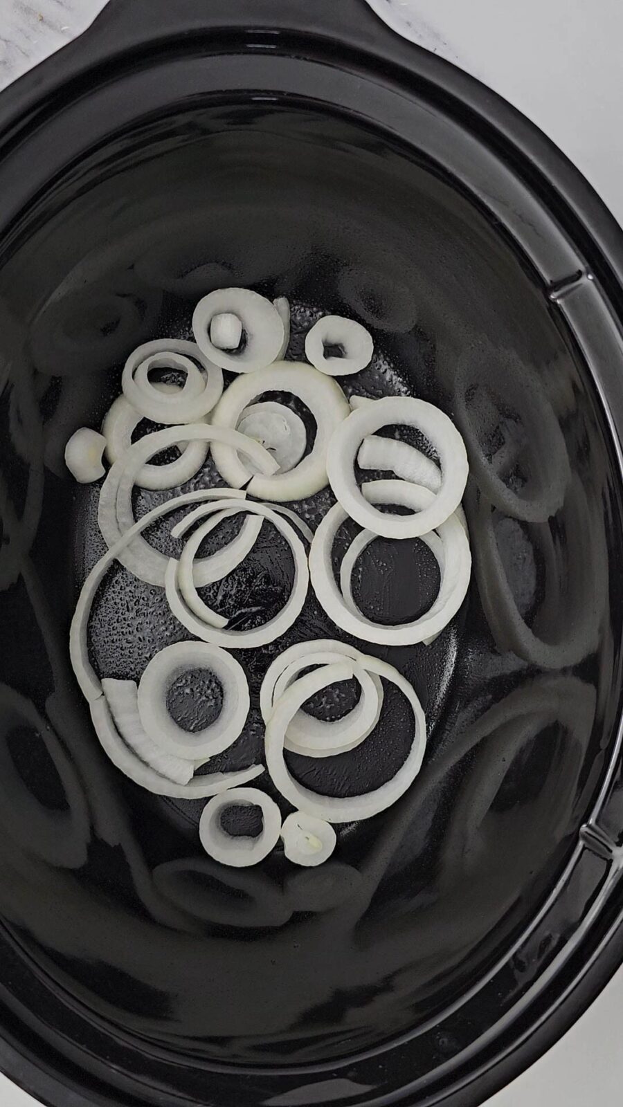 sliced onion rings spread across the bottom of the crockpot