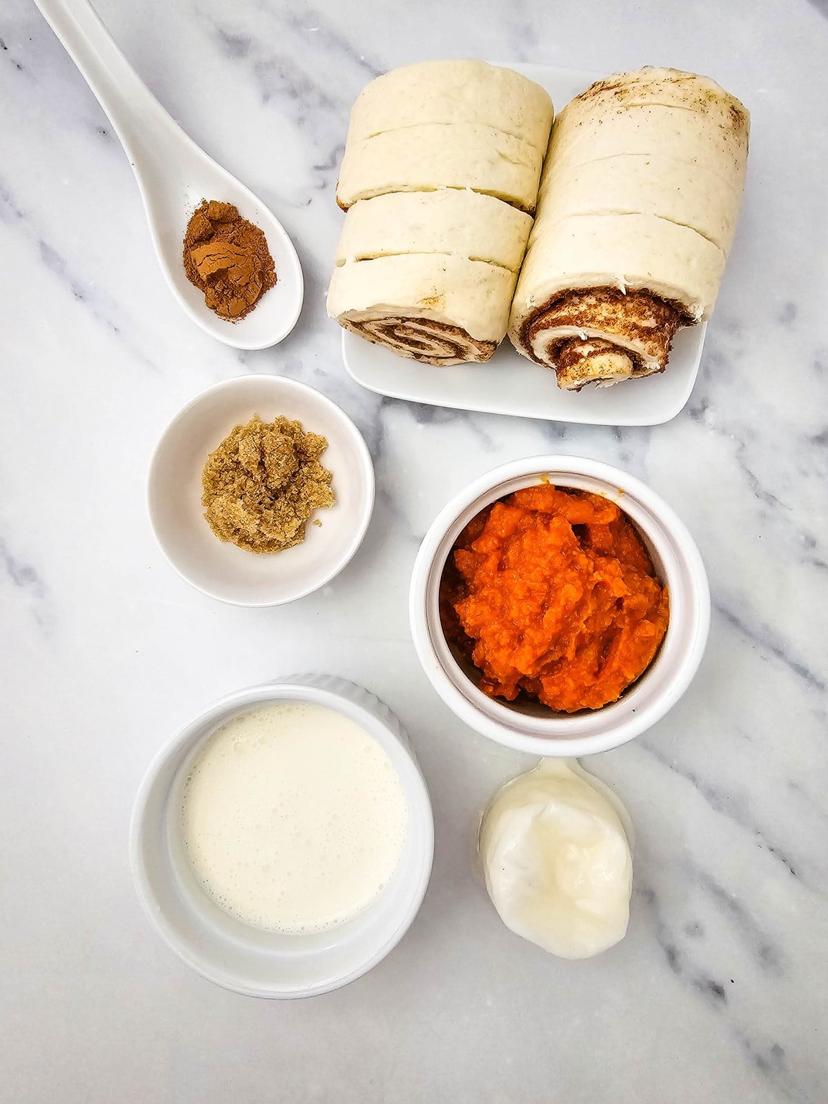 Cinnamon roll dough, pumpkin puree, heavy cream, brown sugar, pumpkin pie spice, and icing laid out on marble