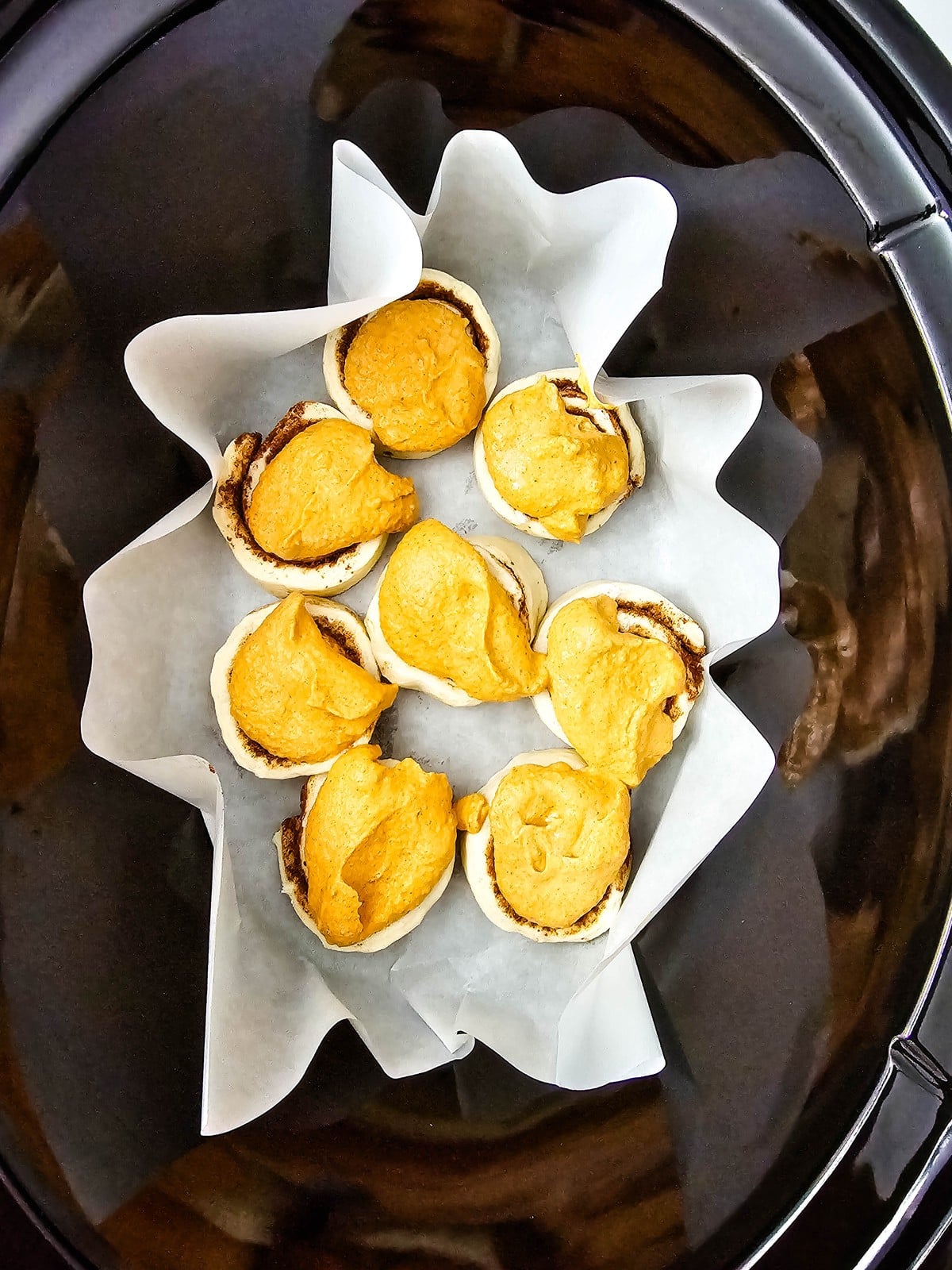 Pumpkin mixture spooned over each raw cinnamon roll in the slow cooker