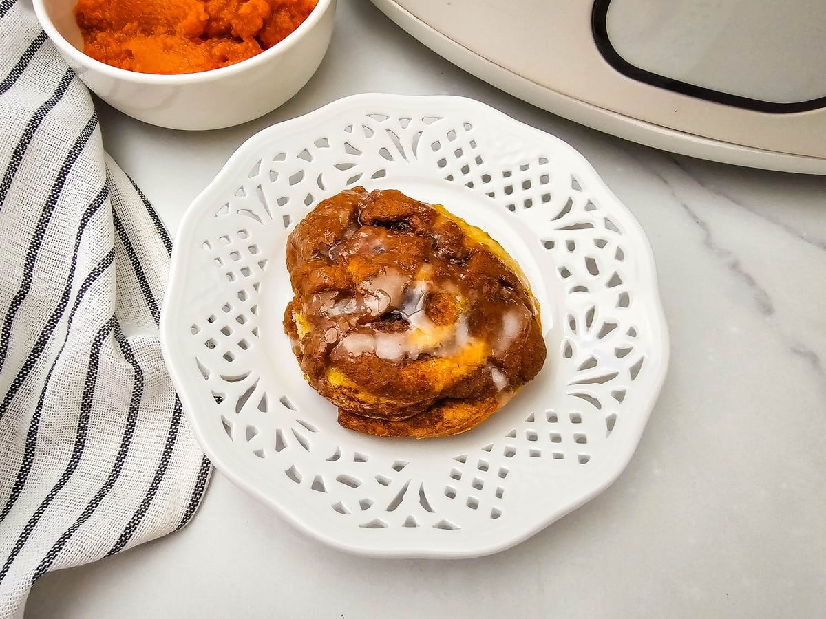 Overhead view of a glazed crockpot pumpkin cinnamon roll on a white scalloped plate