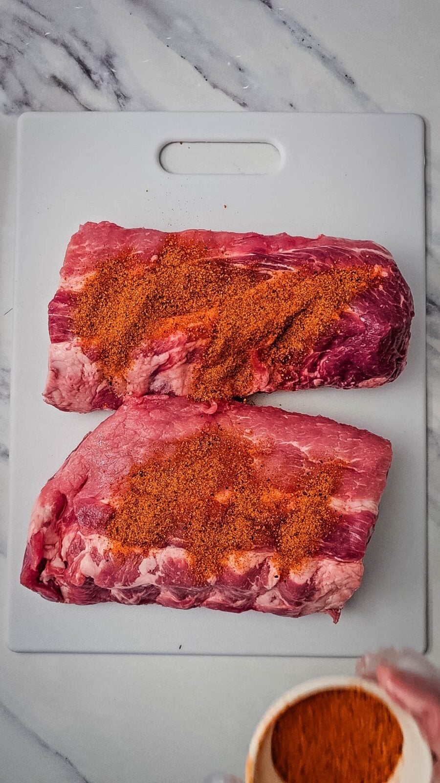 Dry BBQ seasoning sprinkled over two halves of a baby back rib rack on a cutting board