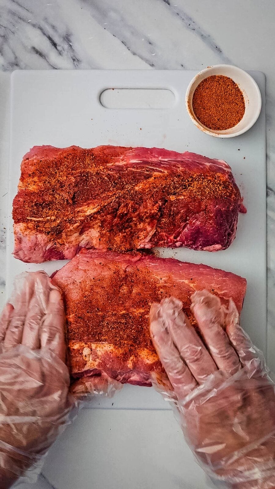 Gloved hands rubbing BBQ seasoning into baby back ribs