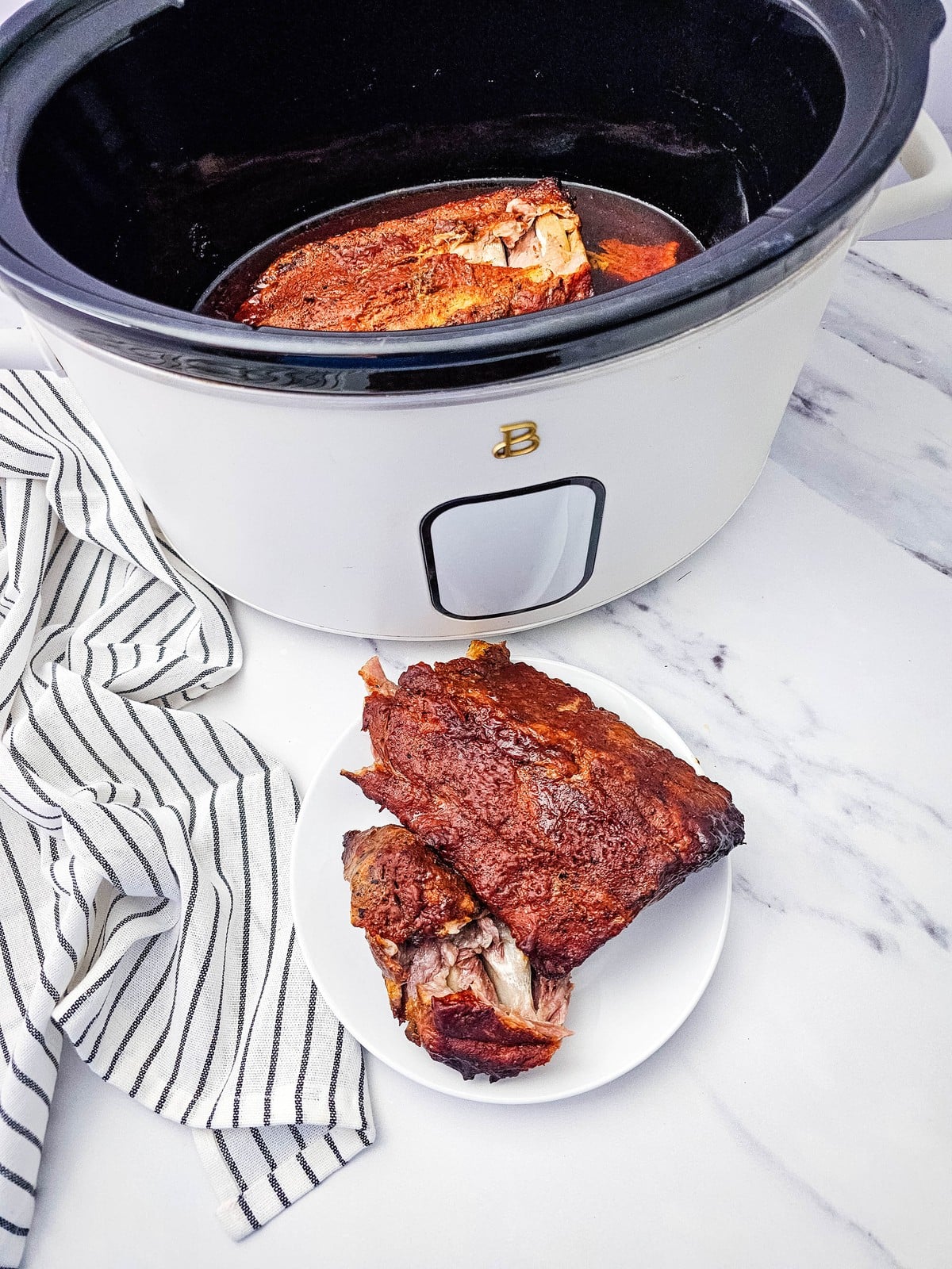 Crockpot ribs served on a plate next to the slow cooker