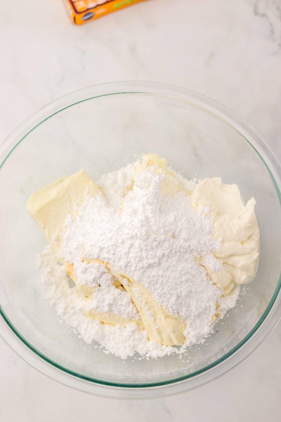Cream cheese blocks and powdered sugar in a glass mixing bowl