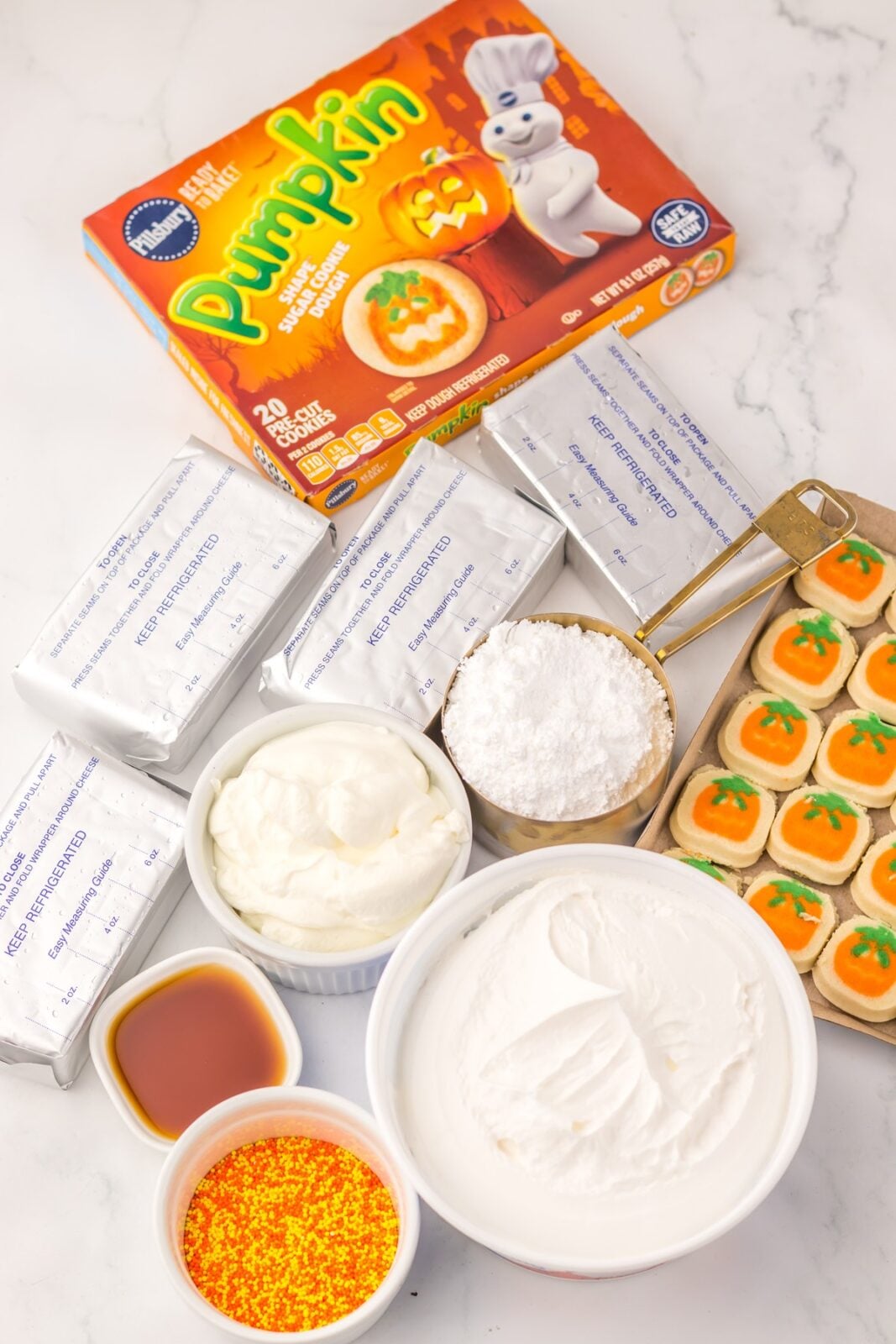 Ingredients for no bake Halloween cheesecake including Pillsbury pumpkin cookie dough, cream cheese, and sprinkles