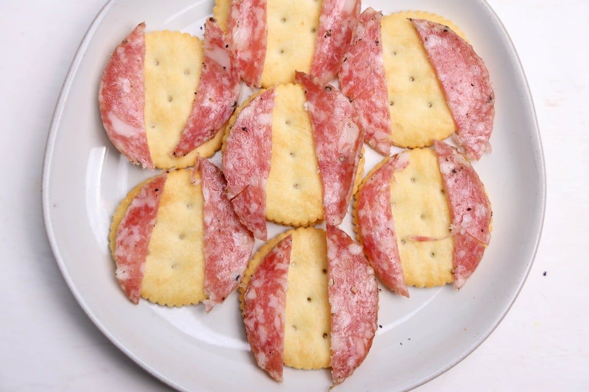 Ritz crackers with peppered salami pieces placed as owl wings on a white plate