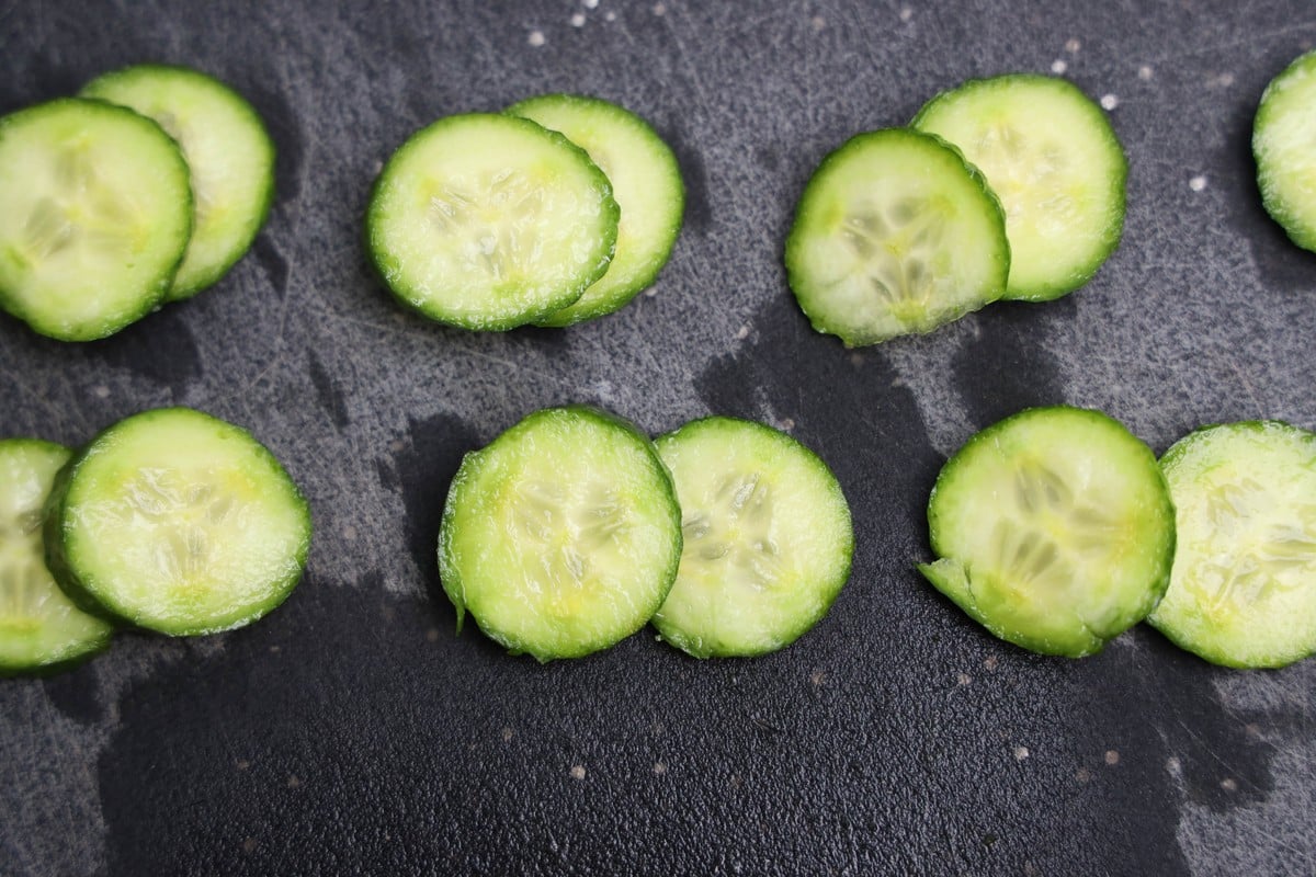 Thinly sliced cucumber rounds on a dark cutting board for owl cracker eyes