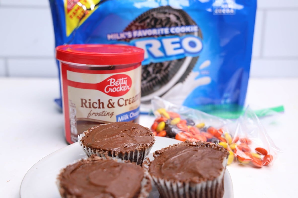 Oreo cookies, chocolate frosting, Reese&rsquo;s Pieces, and frosted chocolate cupcakes on a white counter