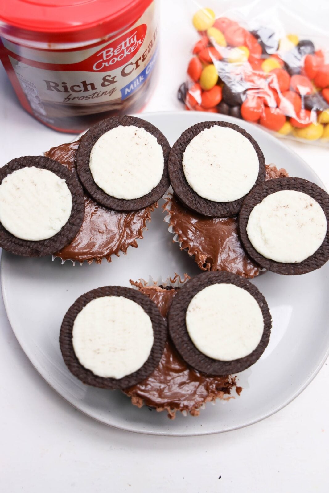 Oreo cookie halves with the cream side up placed on frosted cupcakes as owl eyes