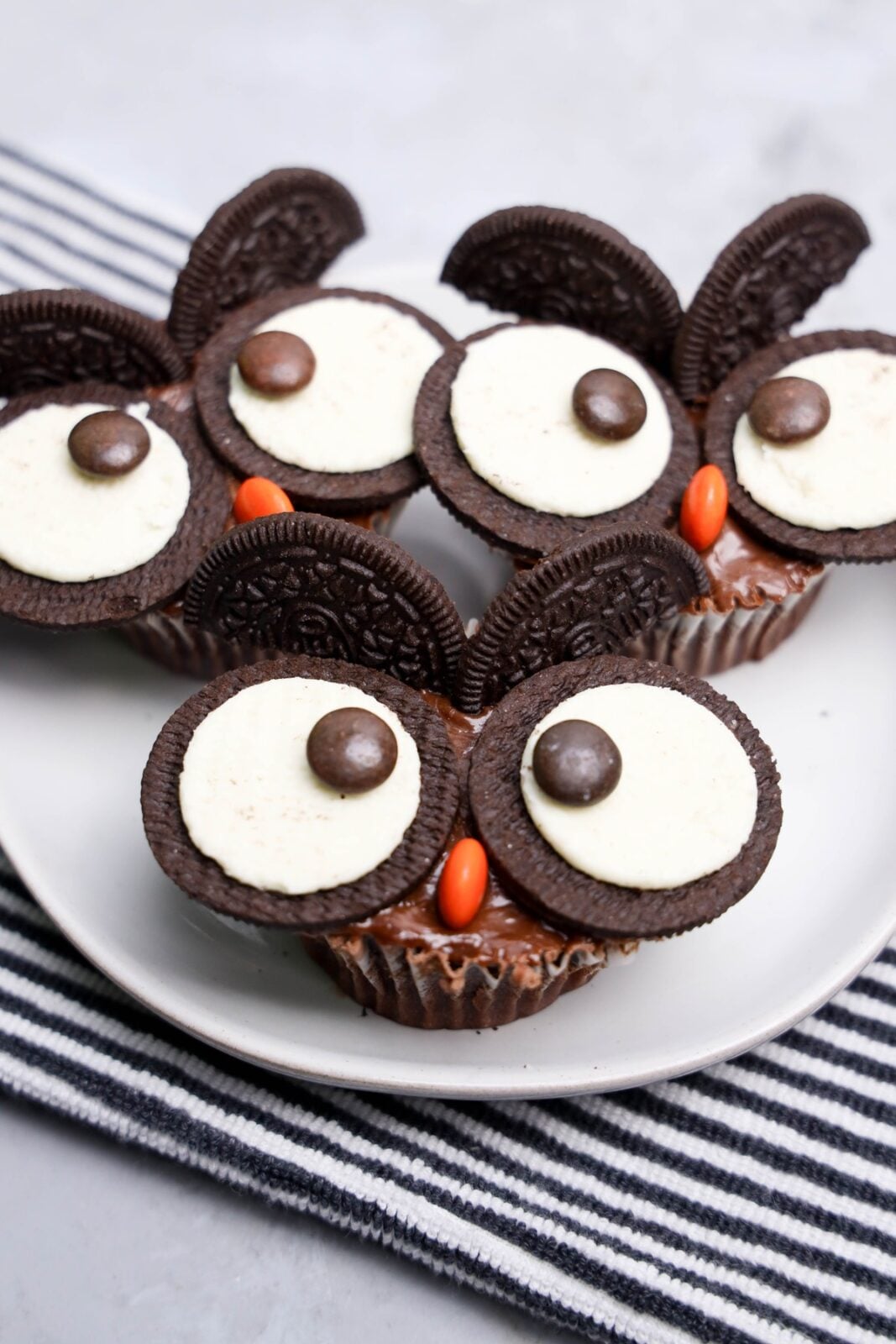 Three owl cupcakes made with Oreo cookies and Reese&rsquo;s Pieces on a white plate