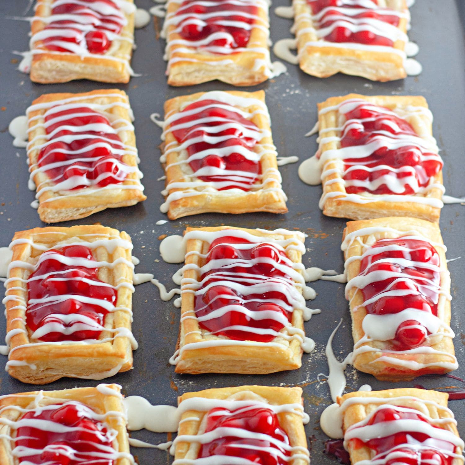 Cherry danishes made with puff pastry, cream cheese and cherry pie filling, drizzled with white icing.