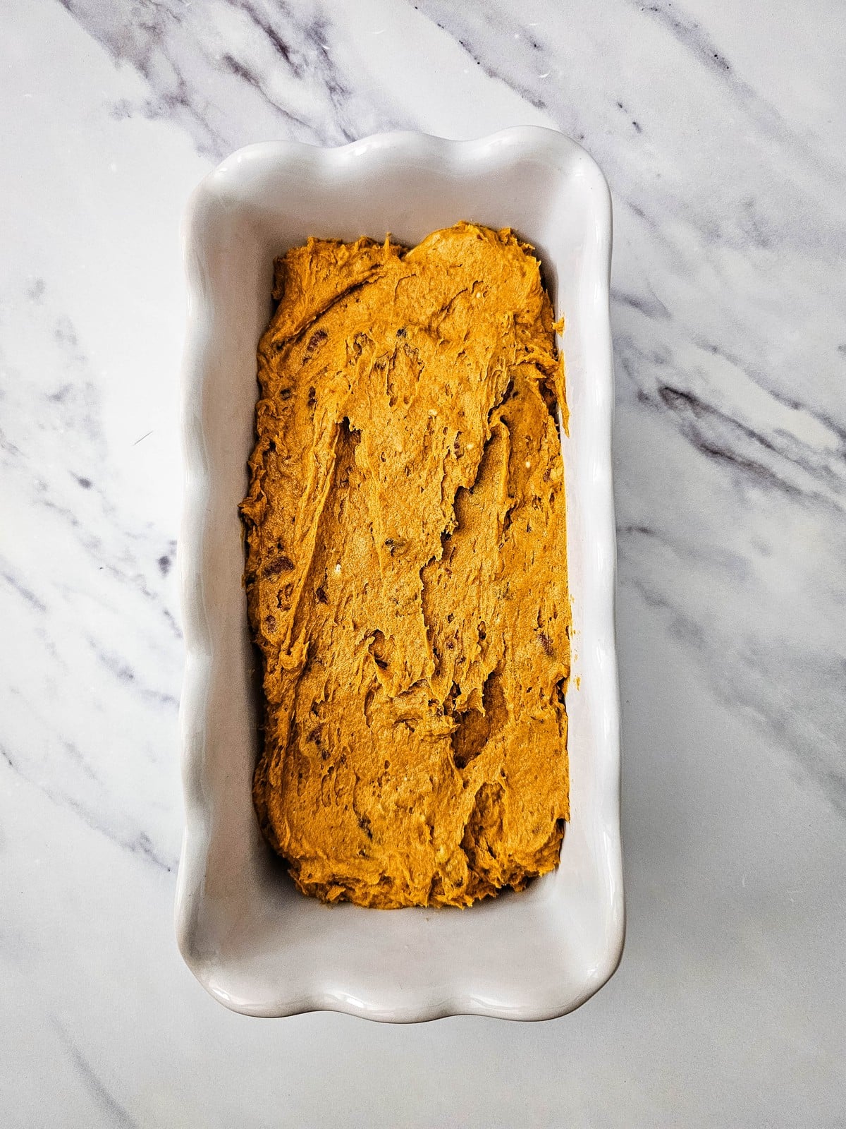 Pumpkin bread batter spread into a white ceramic loaf pan
