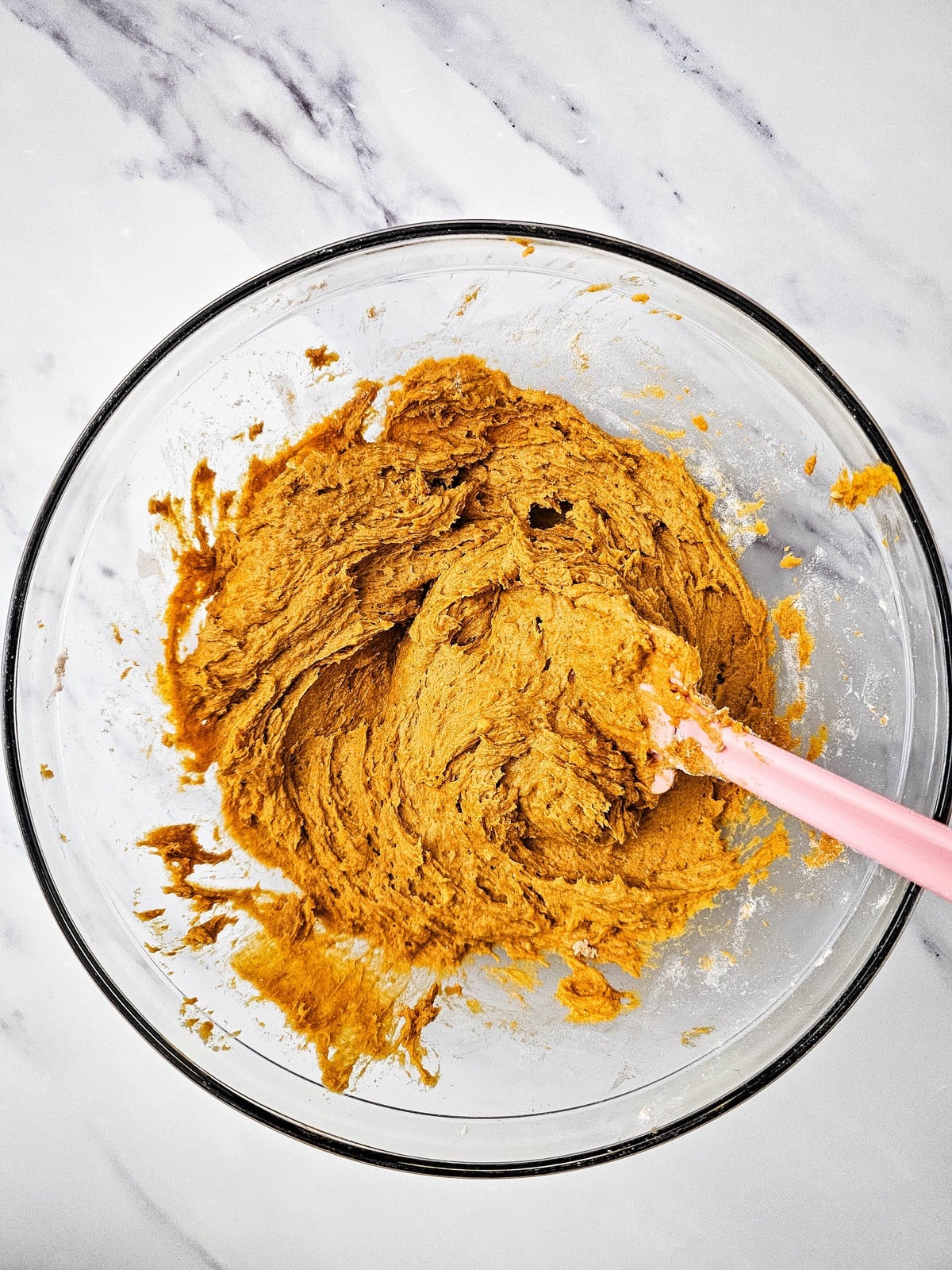 Thick pumpkin bread batter stirred together in a glass bowl with a pink spatula