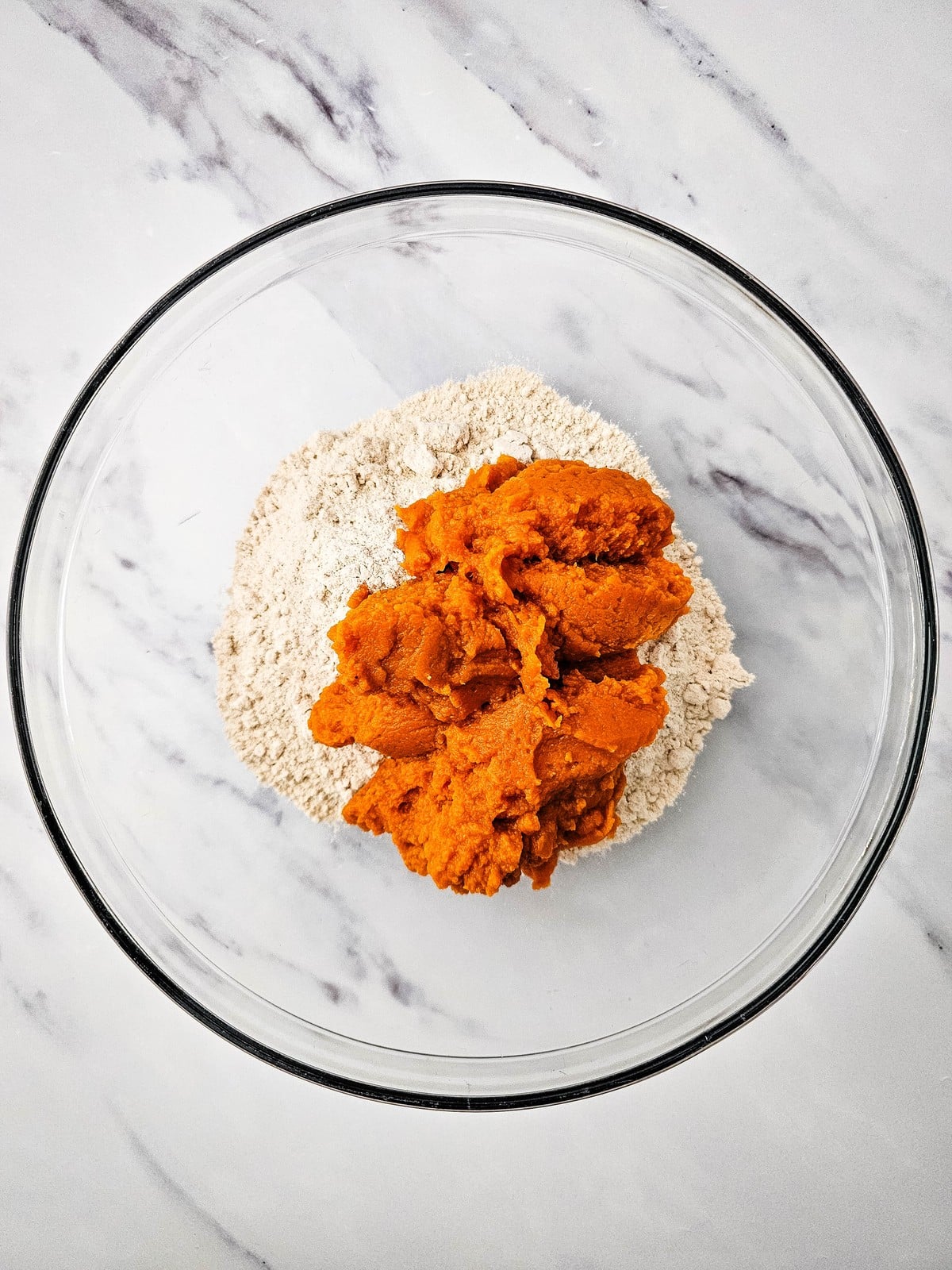 Canned pumpkin puree spooned onto dry spice cake mix in a glass mixing bowl